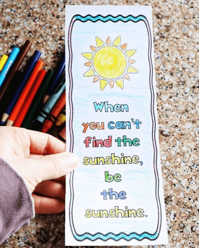Woman's hand holding free printable growth mindset coloring bookmark that says When you can't find the sunshine, be the sunshine.